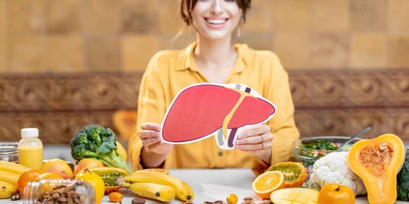 Naine hoiab käes maksa pilti, laual köögiviljad ja puuviljad